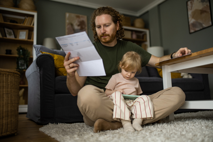 A picture of a father holding a bill and his small child in his lap.